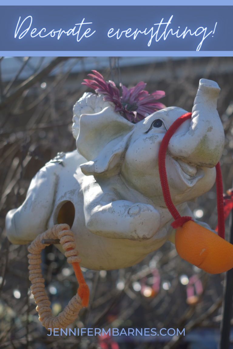 Whimsical elephant statue decorated with an orange basket and Cheerio wreath with the words, "Decorate everything!"